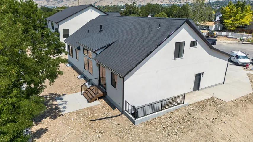 White exterior with a dark roof, featuring multiple windows, concrete patio, and exterior stairs with railing