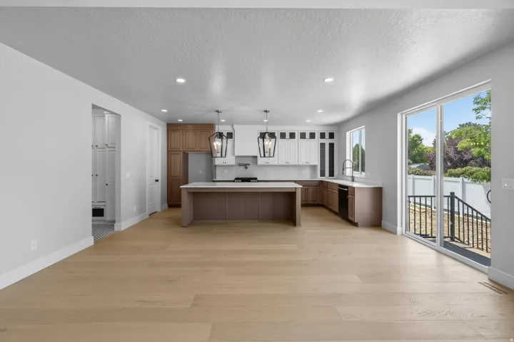 Light wood-finish flooring throughout, modern kitchen with dual-tone cabinetry, central island with seating, pendant lighting, and sliding glass door to the exterior