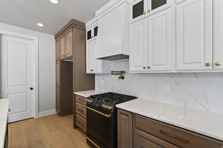 Kitchen featuring light wood-finish flooring, white shaker-style upper cabinetry, dark wood-finish lower cabinetry, white countertops with veining, and a black range with gold-toned accents