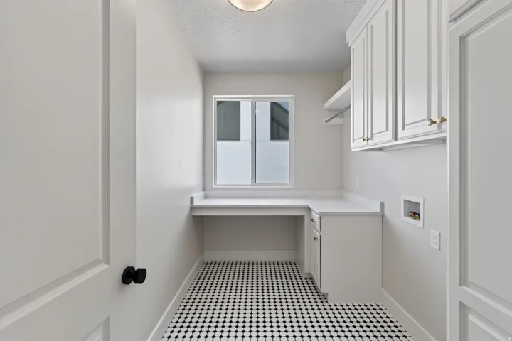 White cabinetry with gold-tone hardware, a dedicated work surface, and black and white patterned floor tiling