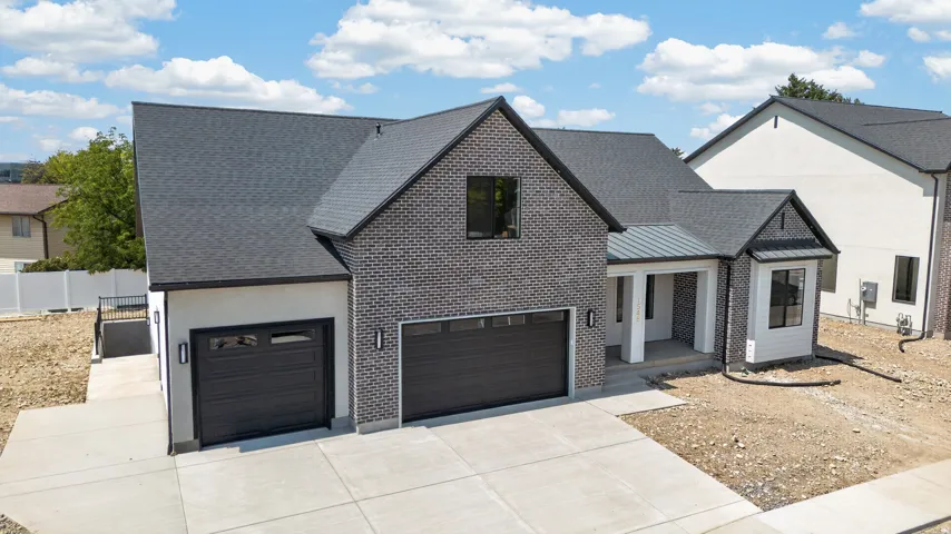Contemporary exterior featuring a dark brick facade, black-framed windows, a covered entry, and two integrated garage bays with opaque panels