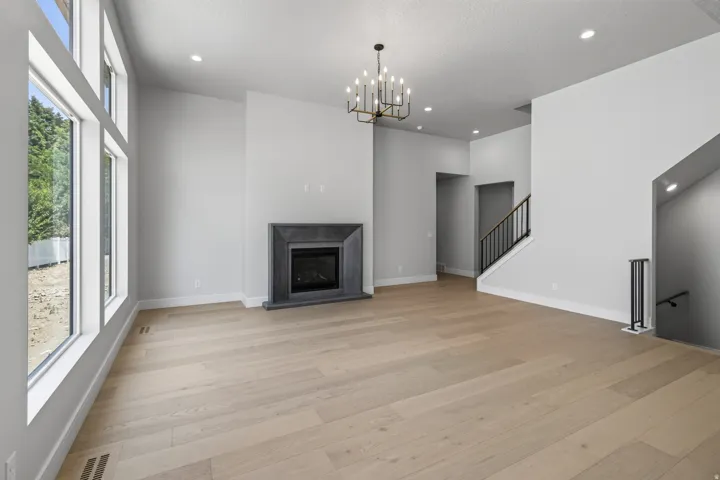 Spacious living area featuring wood-finish flooring, a contemporary fireplace with a dark stone surround, and an elegant chandelier