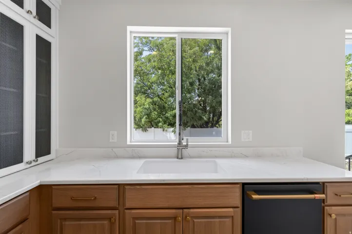White quartz-finish countertops, undermount sink with brushed nickel faucet, wood-finish lower cabinetry, and white upper cabinetry with black mesh inserts