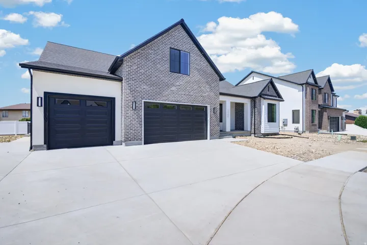 Modern exterior featuring a brick and stucco facade, a dark shingle roof, two garage doors with window inserts, and contemporary exterior lighting