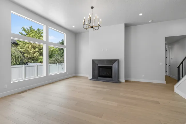 Spacious room featuring light wood-finish flooring, a contemporary chandelier, a built-in fireplace with a dark surround, and large multi-pane windows