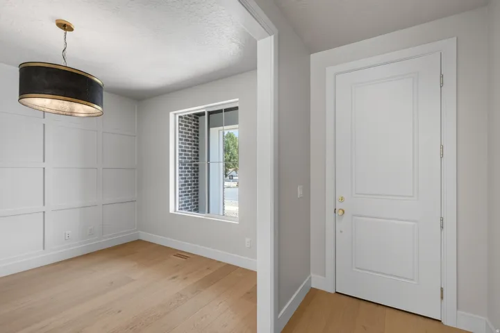 Wood-finish flooring, accent wall paneling, modern drum pendant light, and a white paneled door