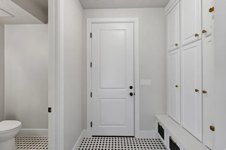 Built-in storage cabinetry with brass hardware, integrated bench seating, and black and white patterned tile flooring