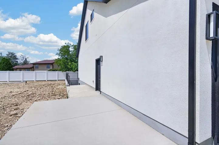 Exterior stucco finish, contemporary black framed windows, concrete patio, exterior lighting fixture, and a white privacy fence