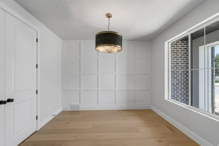 Engineered wood flooring, decorative wall paneling, modern drum pendant light, white trim, and a large window