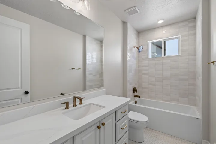 Bathroom featuring white subway tile shower surround, rectangular window, white vanity with gold-tone hardware, integrated sink, and hexagon tile flooring