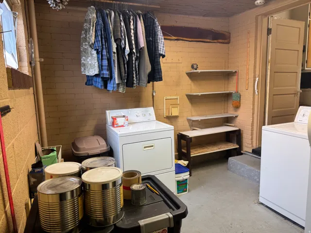 Dedicated laundry area featuring a washer and dryer, painted brick walls, a built-in clothing rack, and integrated wall shelving for storage