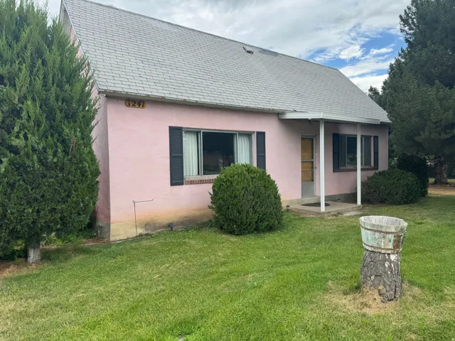 Pink stucco exterior featuring a gabled roof, dark shutters, and a covered entry