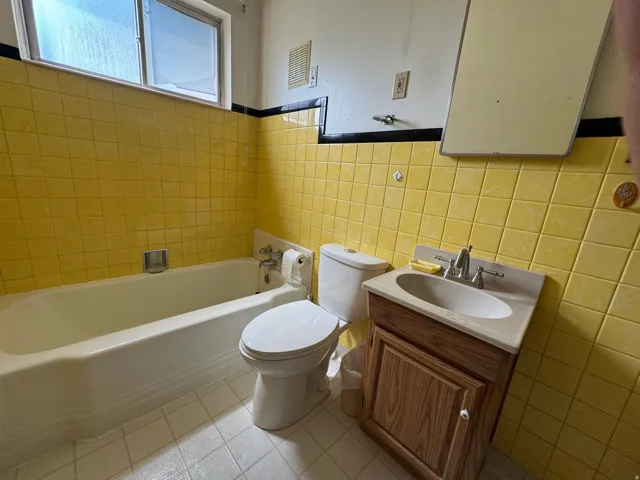 Bathroom featuring yellow wall tiling with a black accent border, a white bathtub, and a window with frosted glass