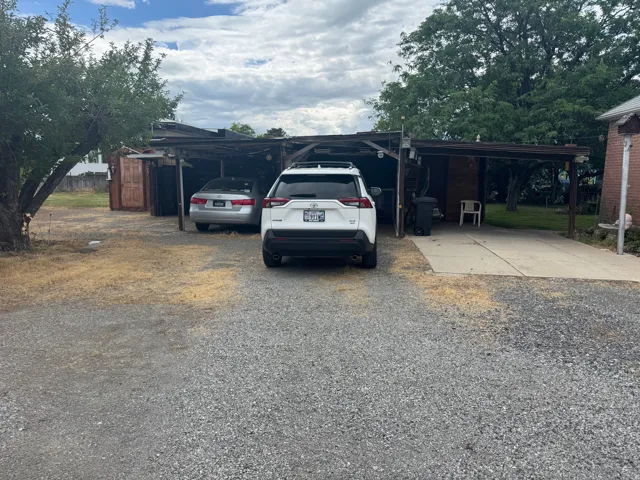 Gravel parking area featuring a concrete driveway and an attached carport structure