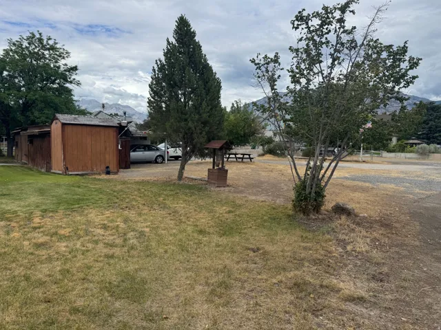 Expansive outdoor space featuring a partial gravel lot, mature trees, a wooden shed, and distant mountain topography