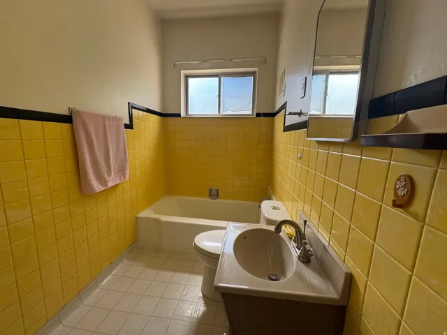Bathroom featuring yellow tiled walls with a black accent border, a white bathtub, a toilet, a vanity with an integrated sink, and a mirrored medicine cabinet