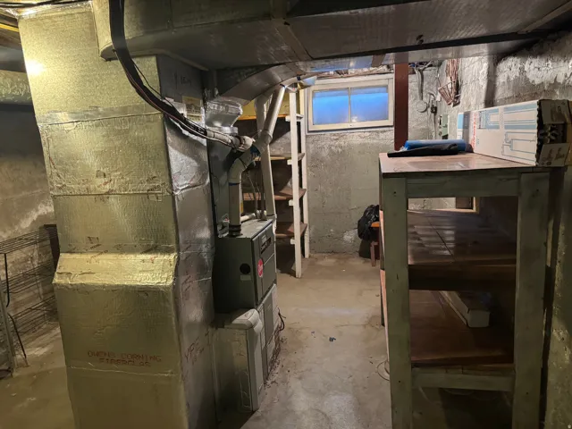 Basement utility area featuring exposed ductwork, concrete walls, a window, and a built-in workbench