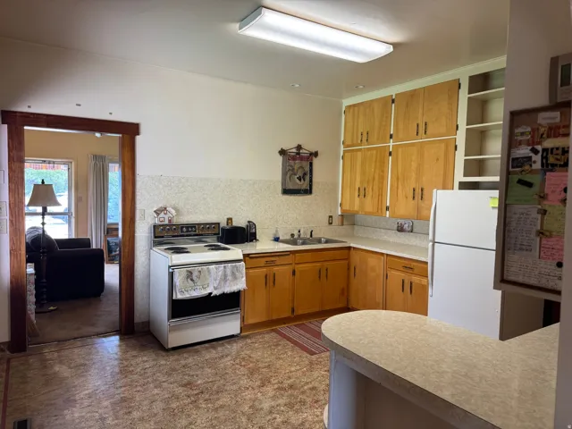 Kitchen featuring light wood cabinetry, a built-in double basin sink, and a white appliance suite