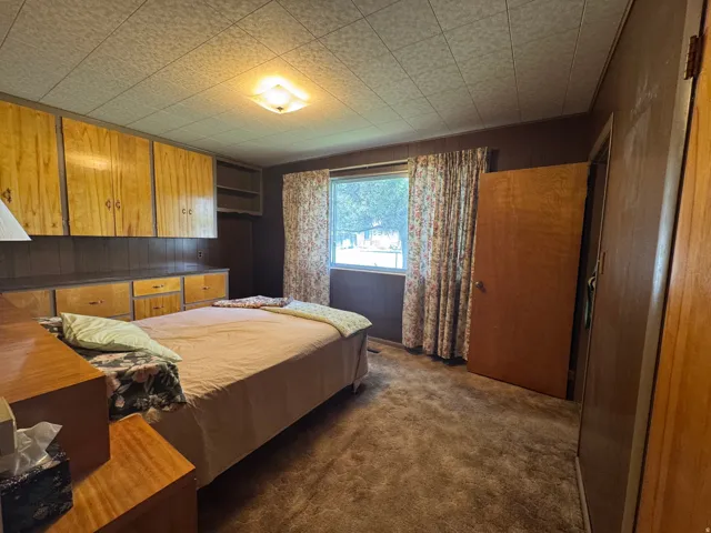 Interior room featuring rich wood-paneled walls, built-in wood cabinetry, a window with exterior visibility, a drop ceiling, and a flush-mount ceiling light fixture