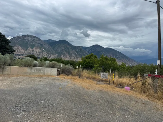 Gravel lot with chain-link fencing and a concrete retaining wall, featuring a mountainous backdrop