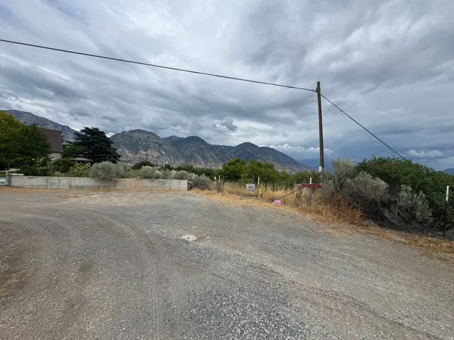 Gravel lot featuring a concrete retaining wall, mature trees, and mountainous terrain in the background