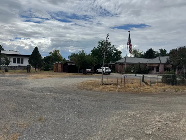 Expansive gravel parking area featuring multiple outbuildings, mature trees, and a flagpole