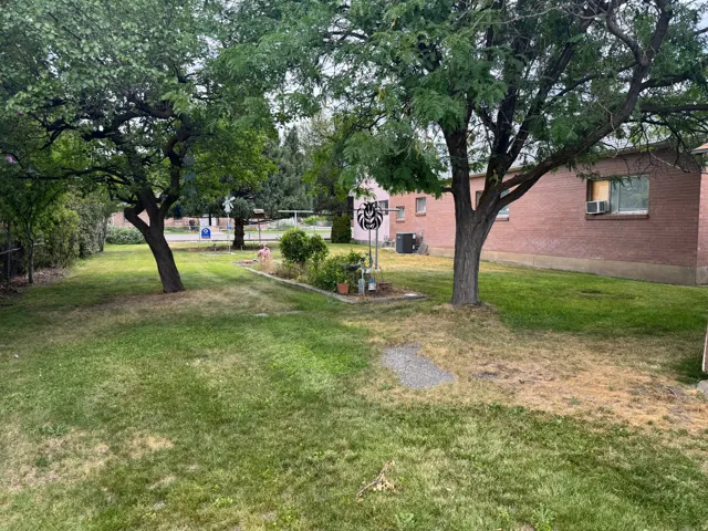 Spacious backyard featuring mature trees, green lawn, a landscaped garden bed, and a red brick exterior