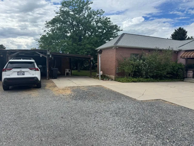 Brick exterior with a gray shingle roof, accompanied by a gravel driveway and concrete parking areas