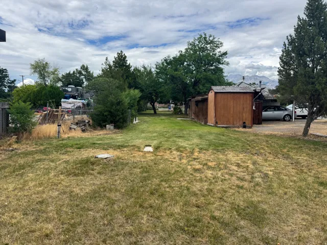 Expansive outdoor space featuring a partial gravel parking area, mature trees, and a wood-sided storage shed
