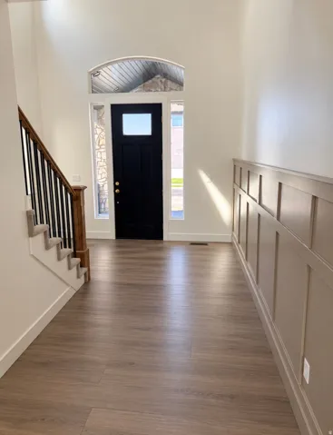 Foyer featuring wood-finish flooring, a two-story entryway, wainscoting, an arched transom window, and a staircase with wood newel posts and black balusters