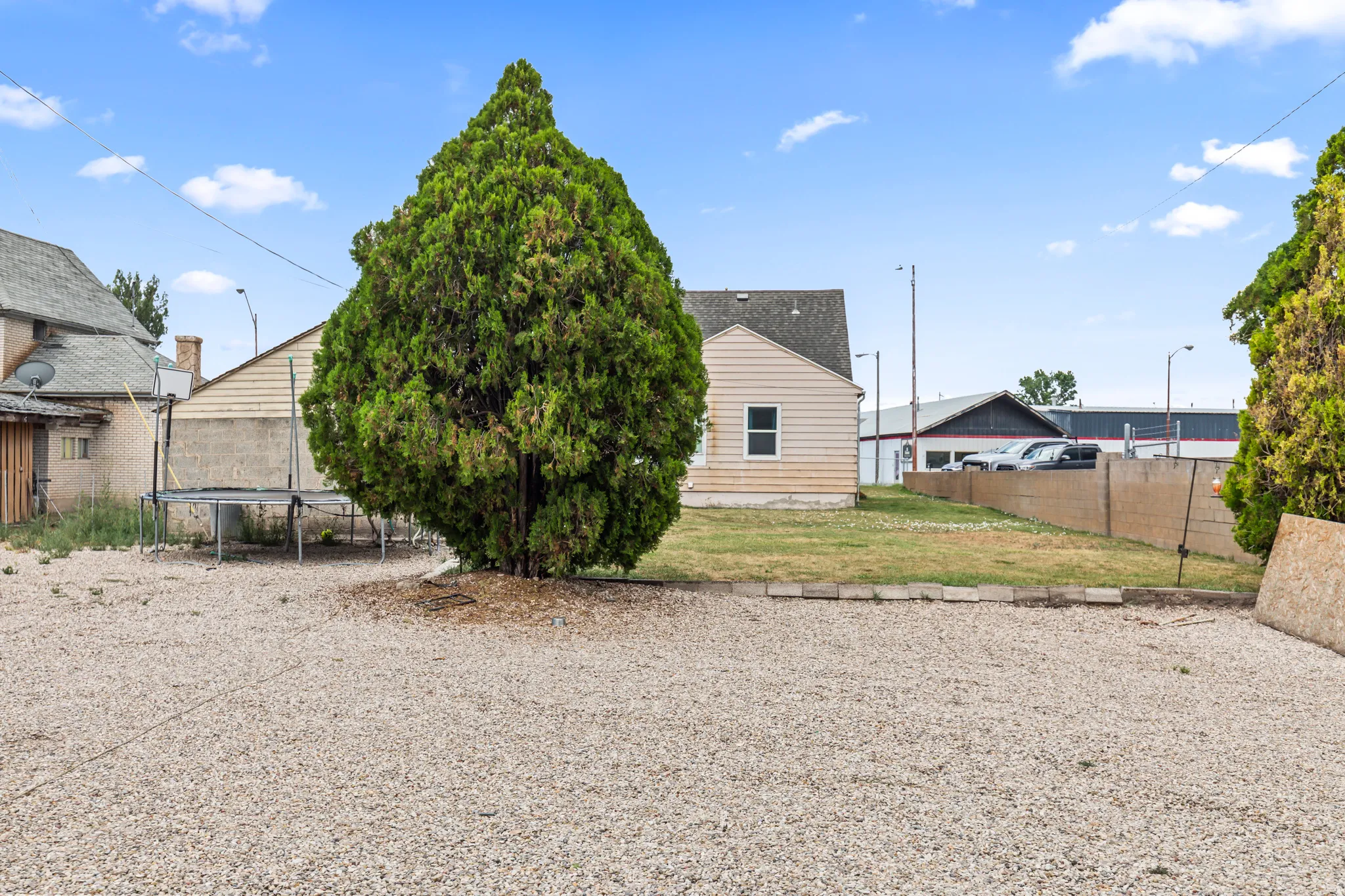 Expansive gravel yard with a large established tree and a grassed area