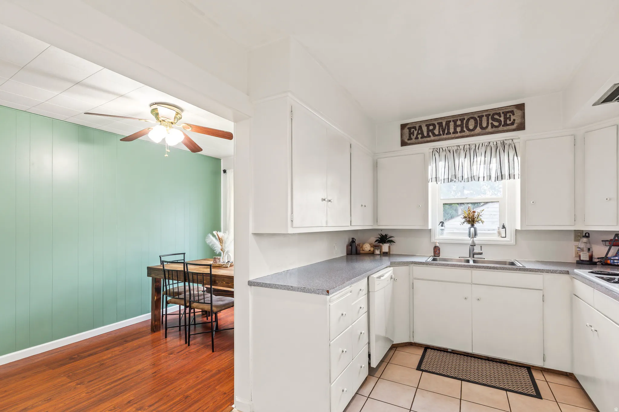 White kitchen cabinetry with dark countertops, a dual-basin sink, and tile flooring