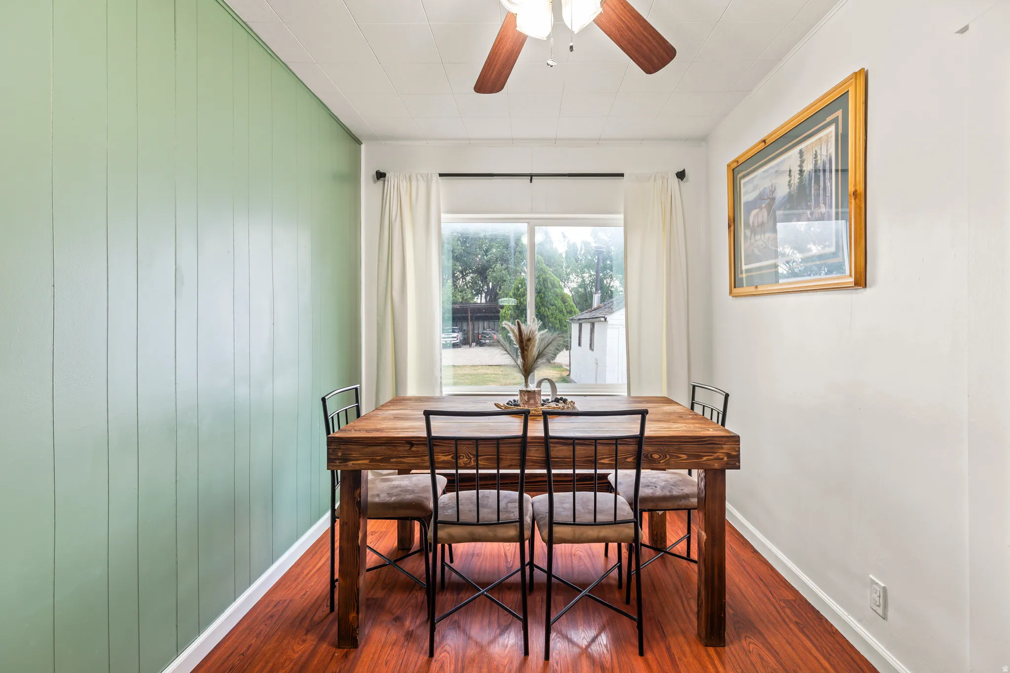Dining space featuring a picture window, wood-finish flooring, a paneled accent wall, and a ceiling fan with light fixture