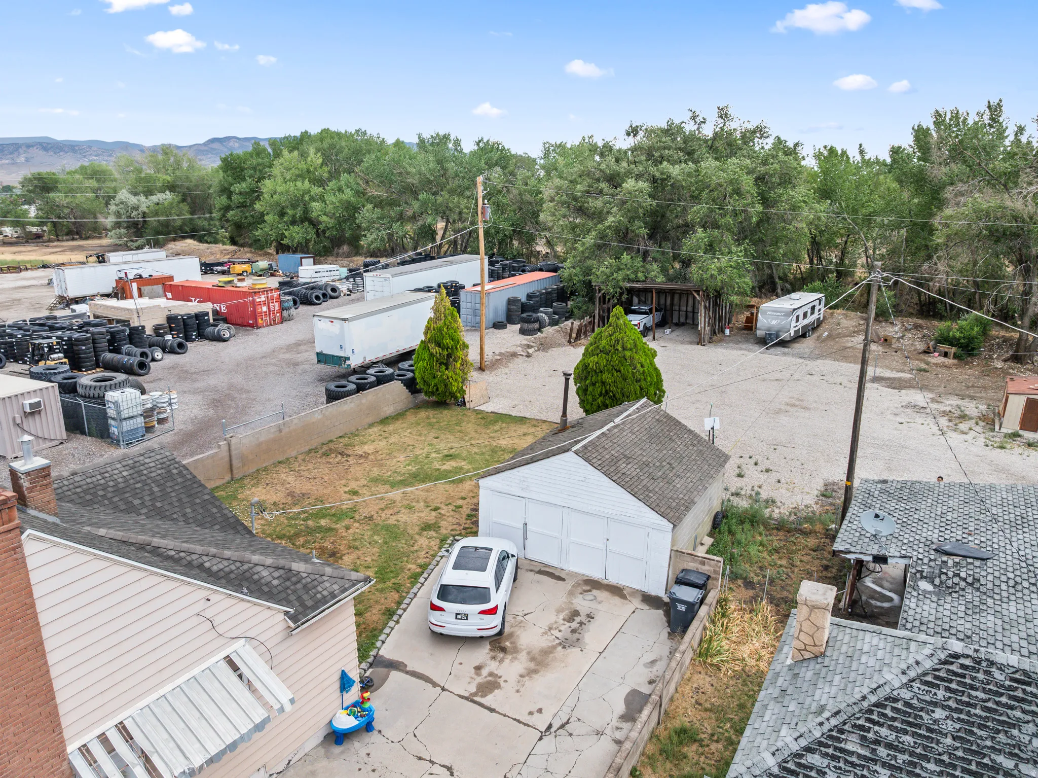 Expansive outdoor area featuring a gravel lot, mature trees, and a detached structure with a pitched roof