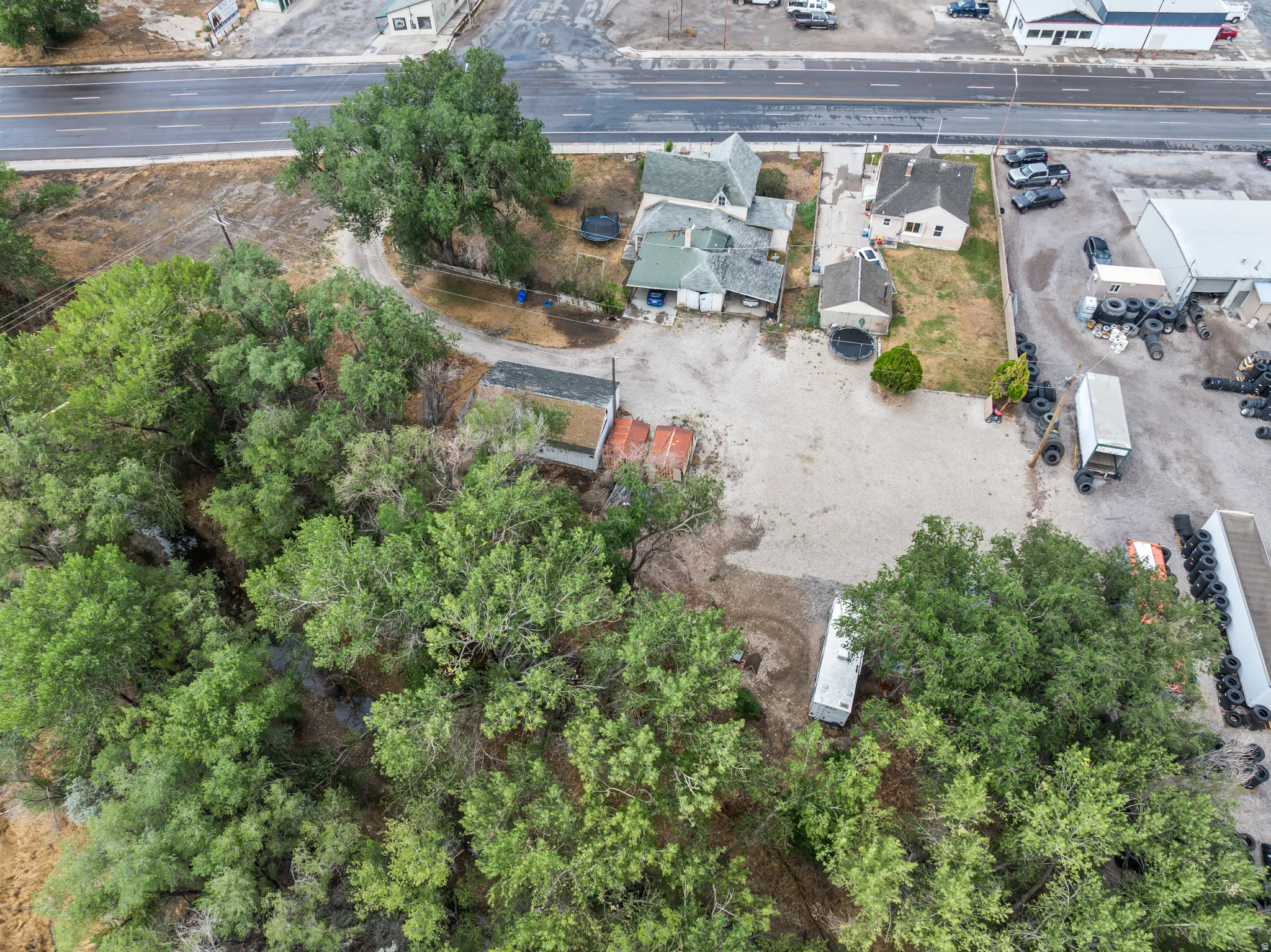 Expansive property featuring mature trees, multiple outbuildings, and a gravel lot