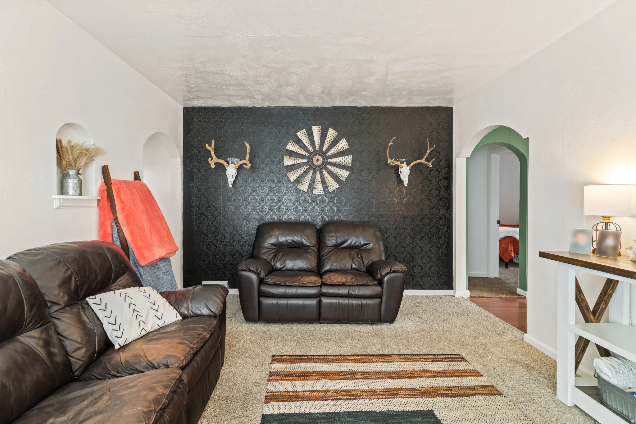 Living area featuring a textured accent wall, light-colored carpeting, white wall finishes, two arched wall niches, and an arched doorway