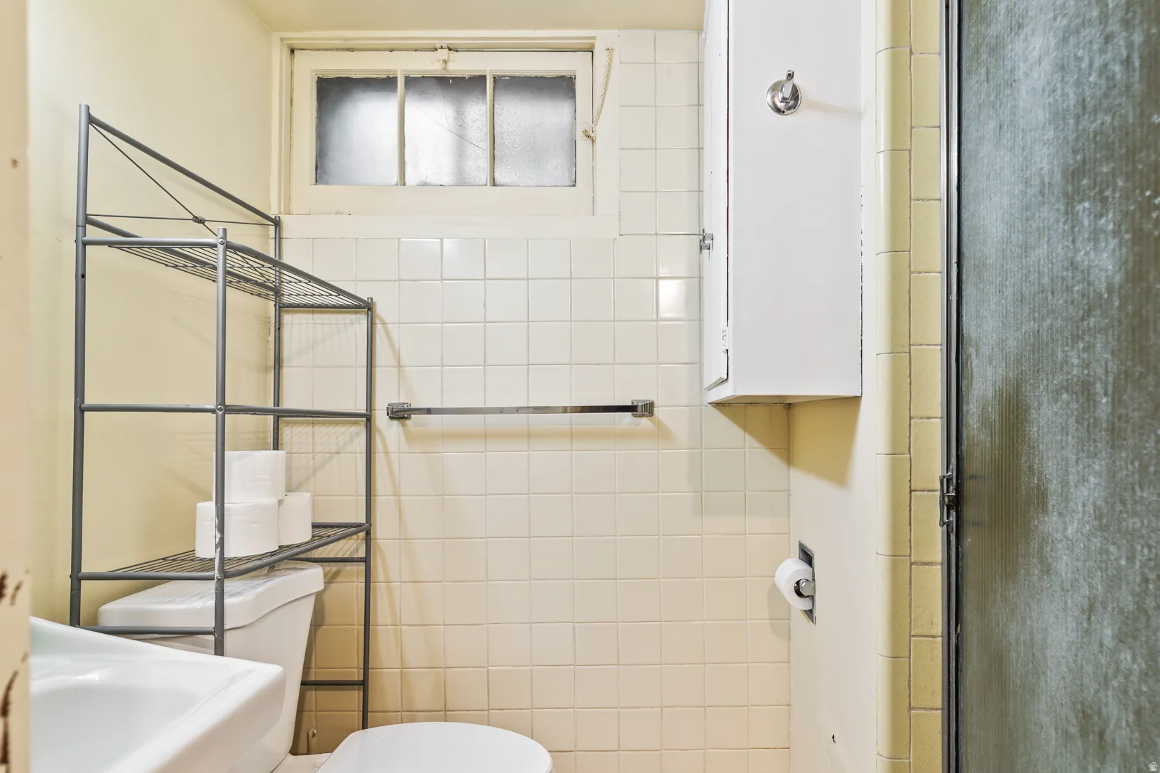 Bathroom featuring white square tile walls, a window with obscure glass, and a wall-mounted storage cabinet