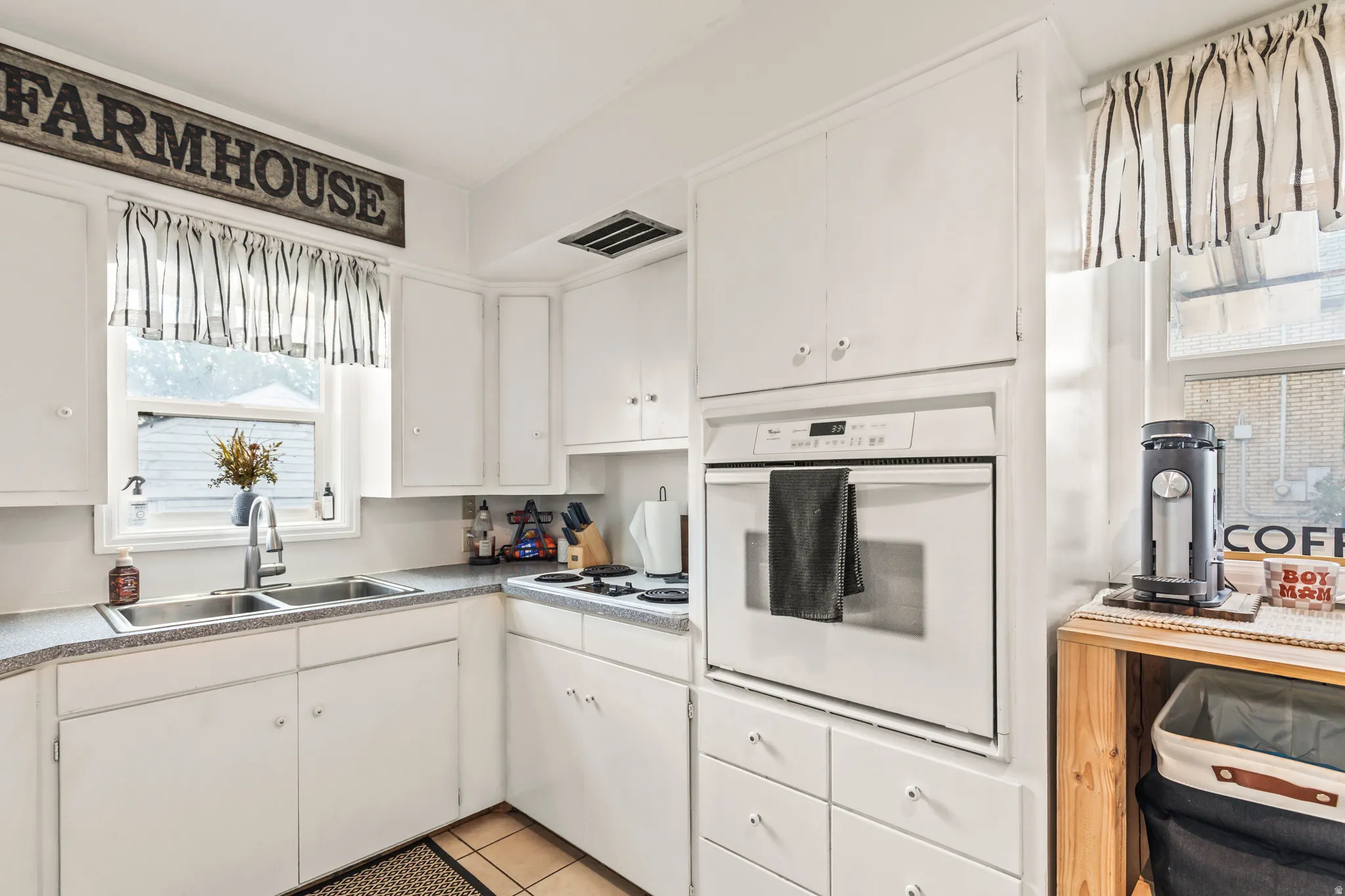 Kitchen featuring white cabinetry, a double basin stainless steel sink, built-in wall oven, and light-colored countertops