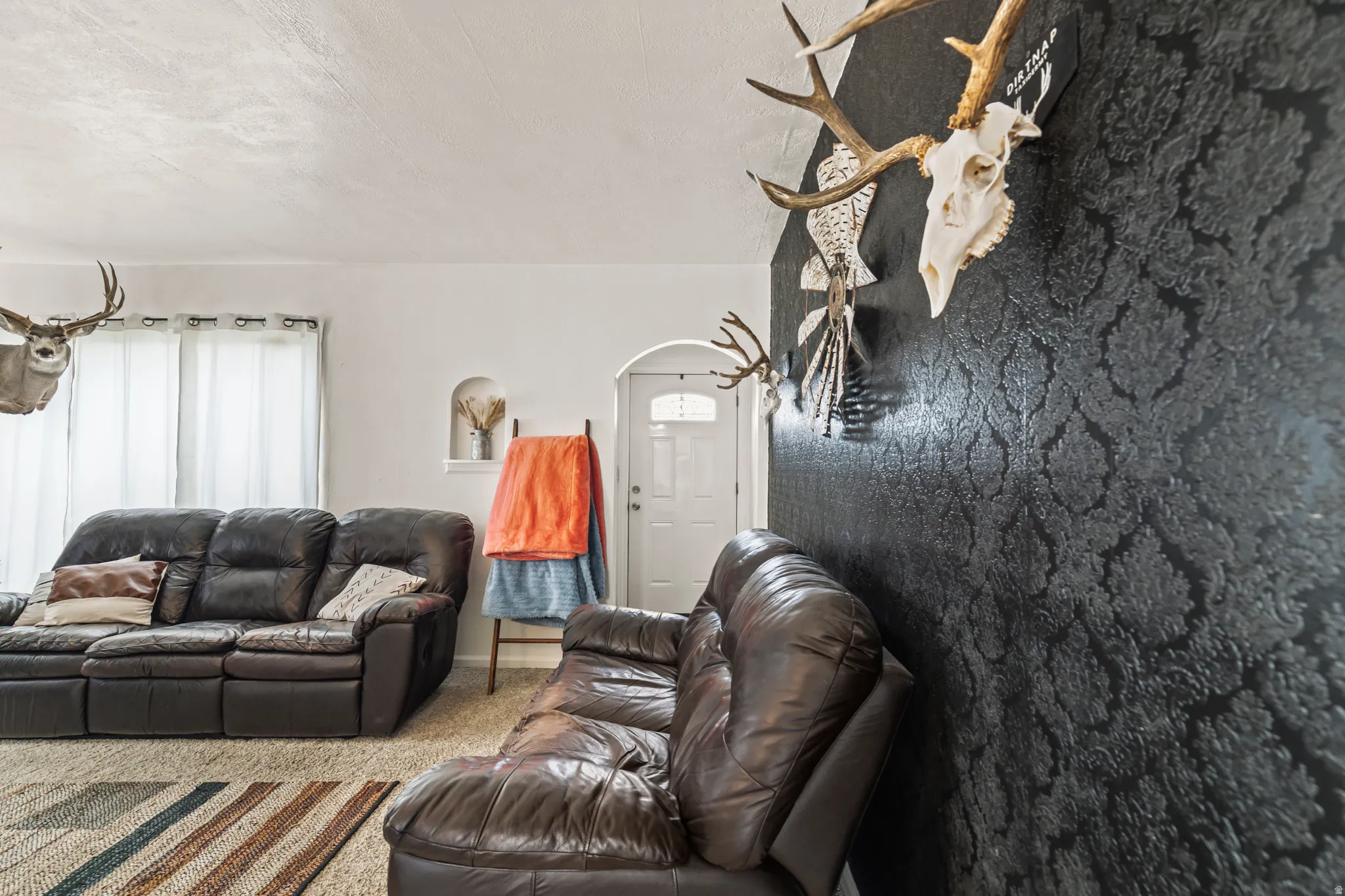 Living area featuring a textured accent wall and light-colored carpeting