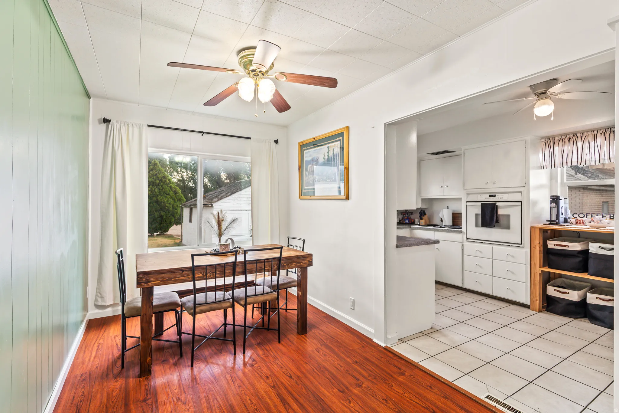 Open-concept living area featuring wood-finish flooring, a ceiling fan with light fixture, and a large window providing outdoor views