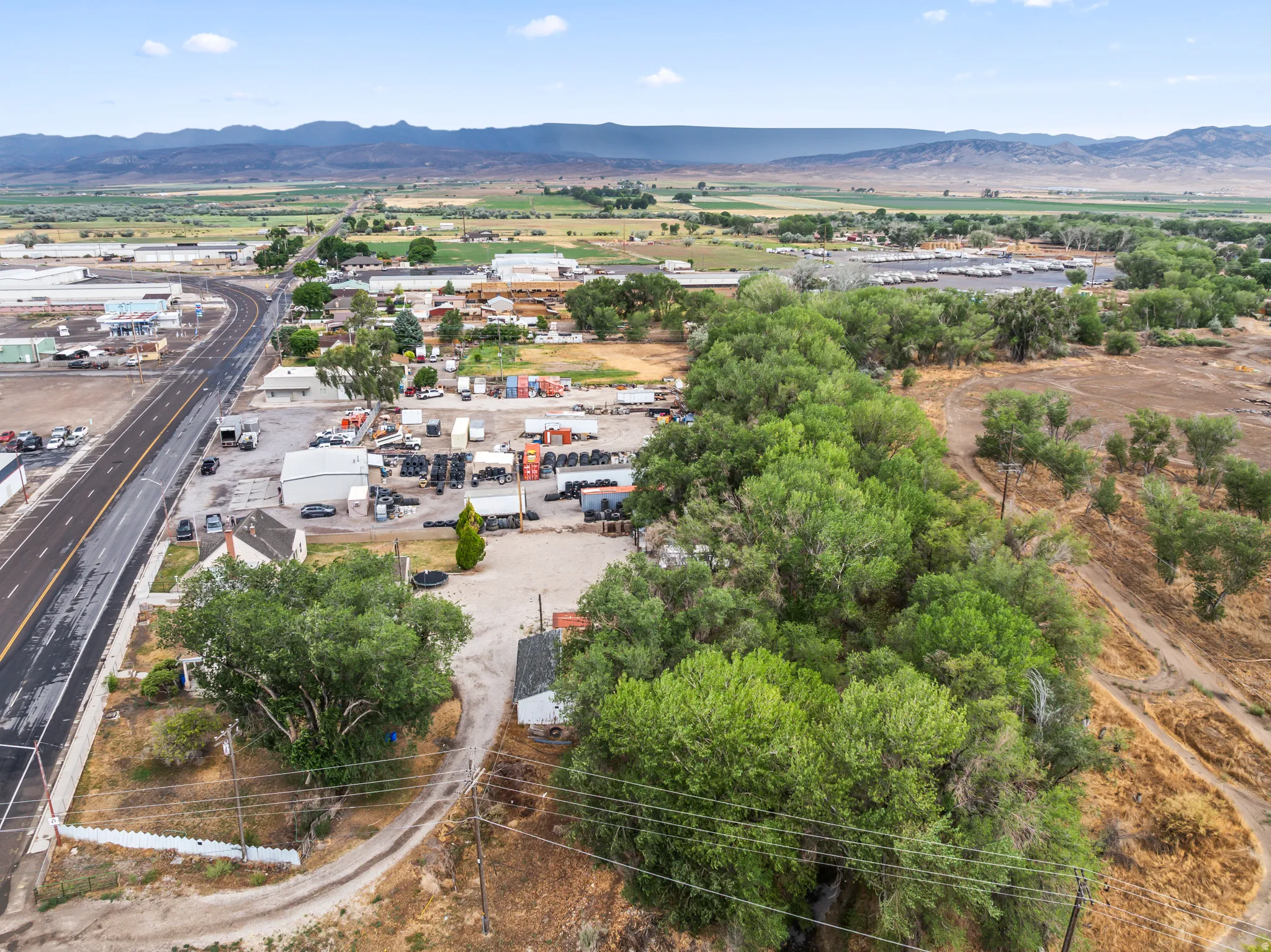 Aerial perspective showcasing an expansive property with a single-story structure, multiple auxiliary buildings, and a large, paved parking area