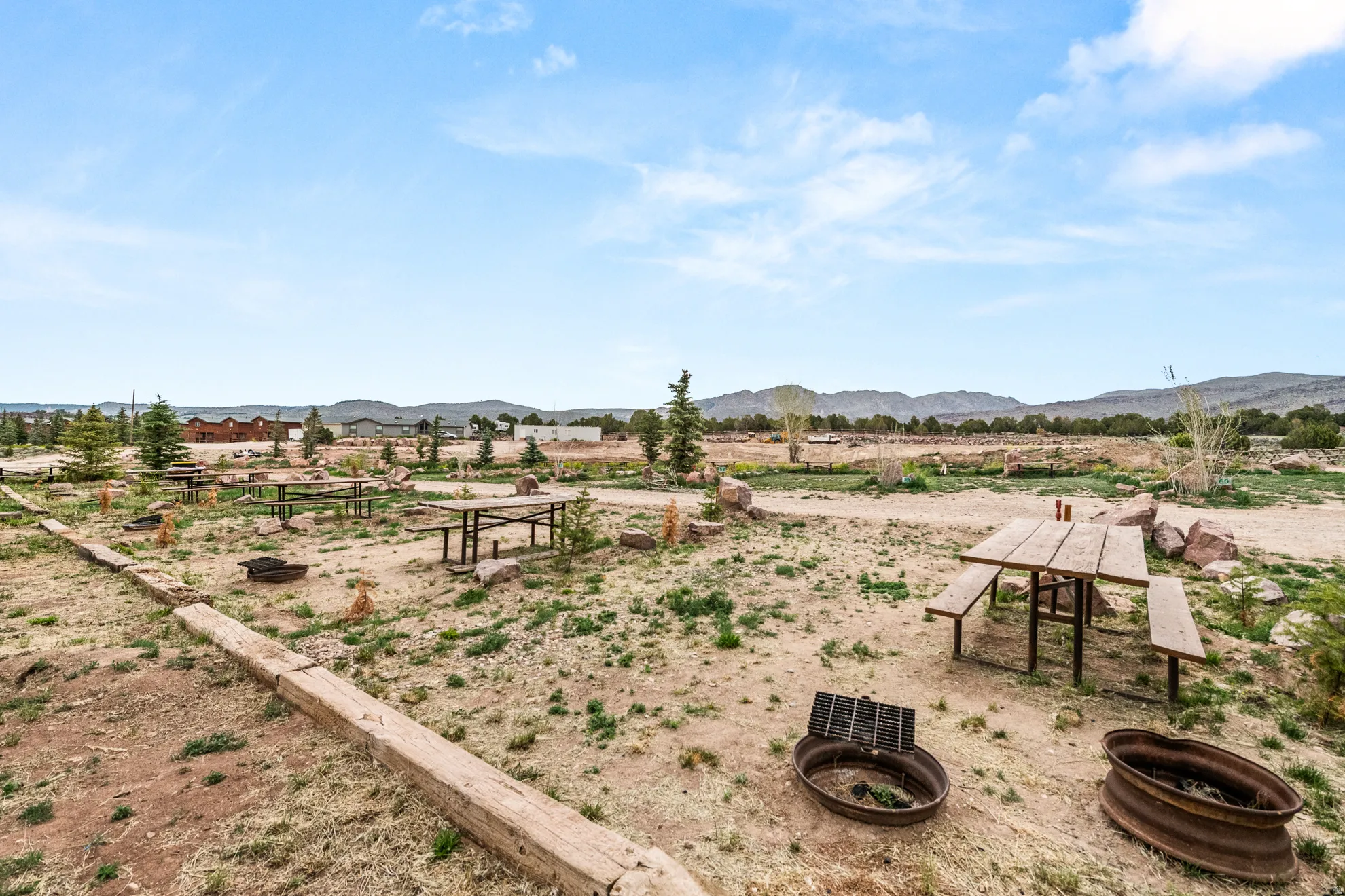 Expansive open area with multiple picnic tables, fire rings, and natural landscaping