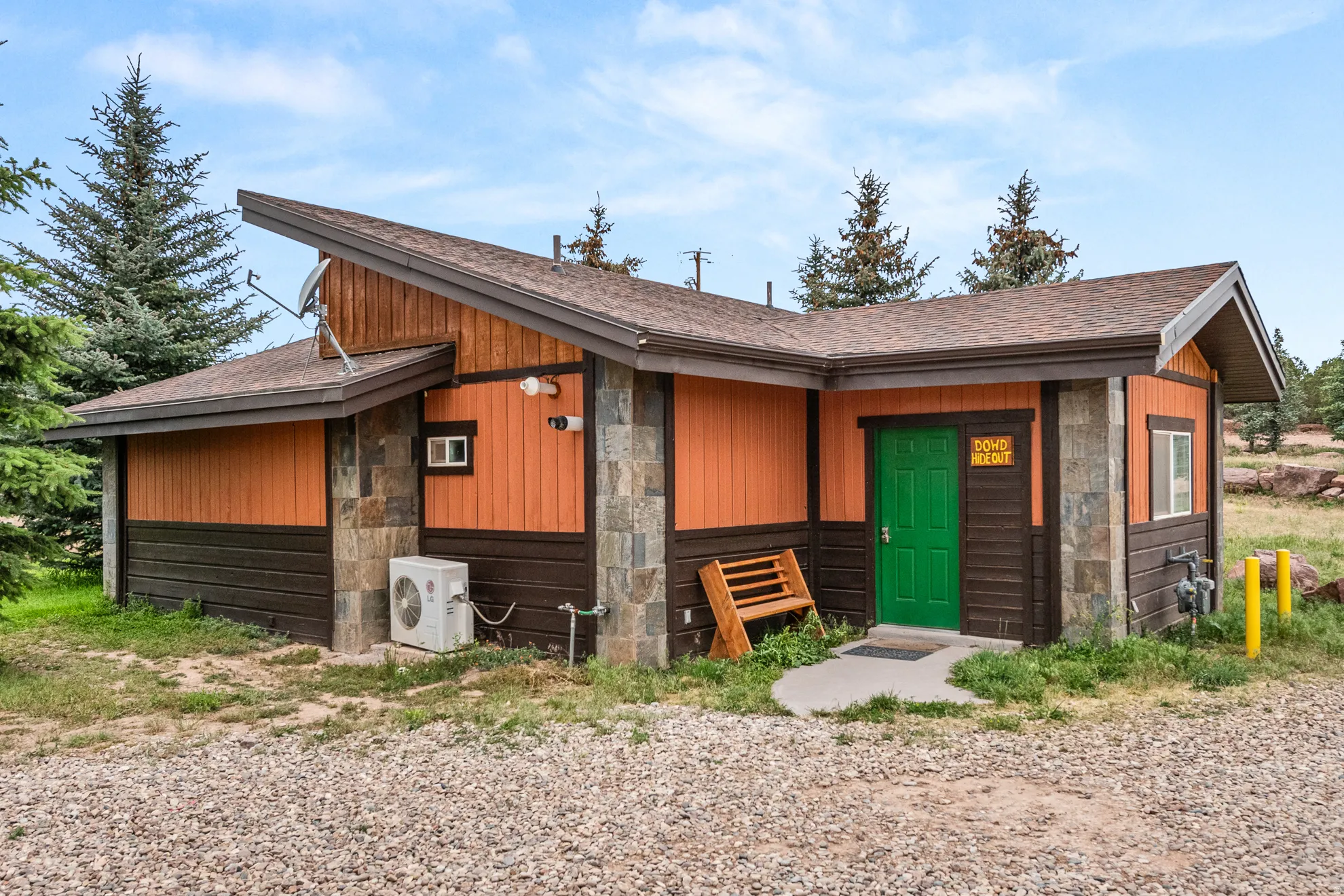 Exterior featuring stone accents, orange and dark brown siding, a green entry door, and a brown shingle roof