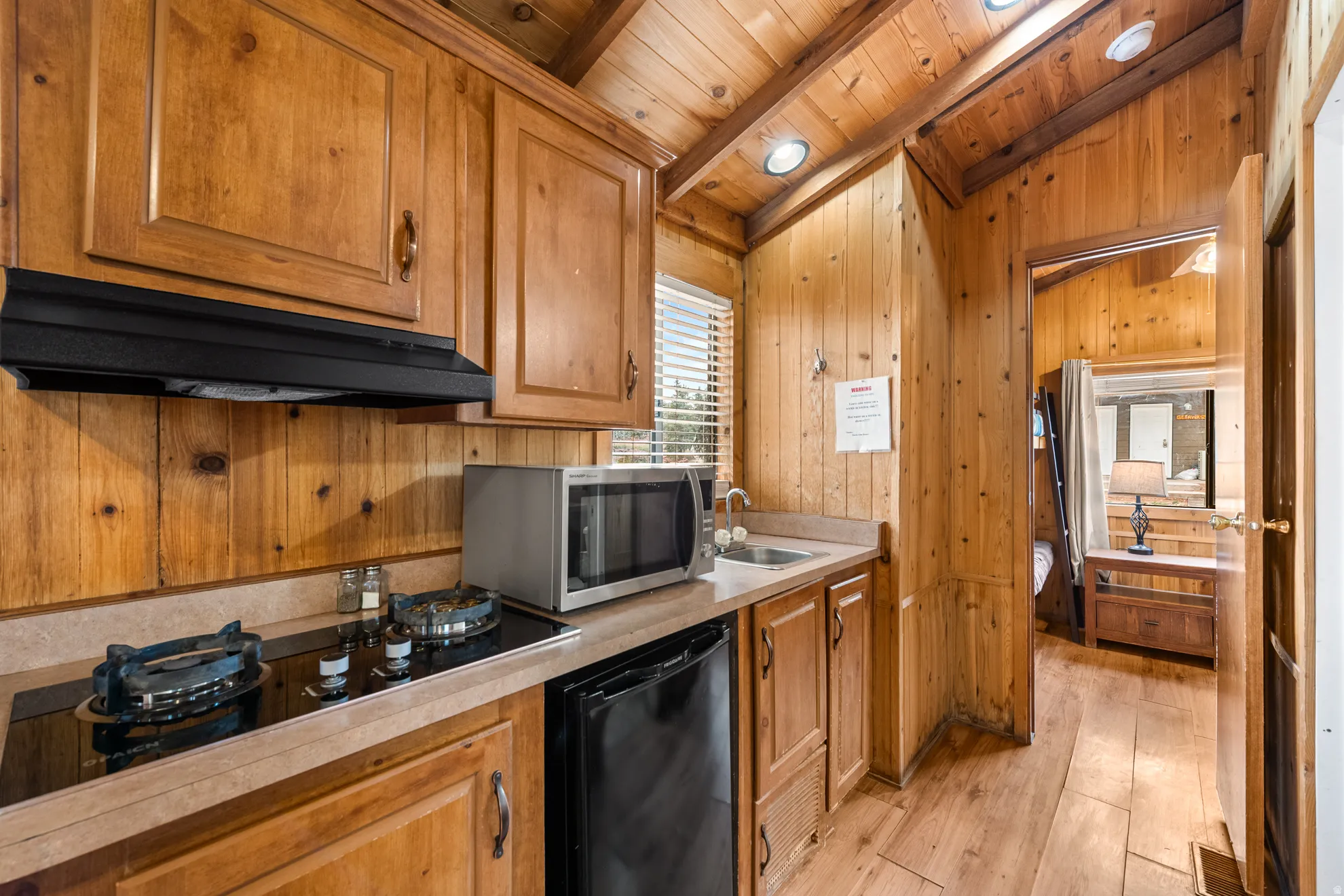 Compact kitchen featuring wood paneling, wood-finish flooring, recessed lighting, and a built-in cooktop