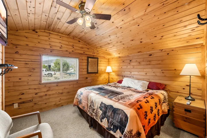 Wood-paneled room featuring a vaulted ceiling with exposed wood beams and a ceiling fan