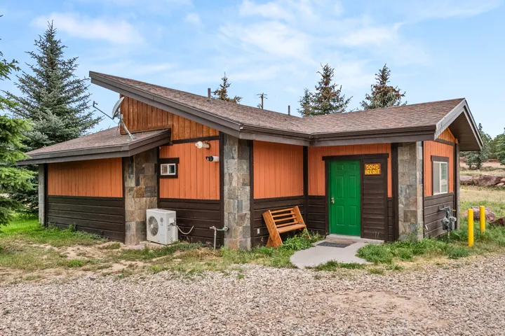 Exterior featuring stone accents, orange and dark brown siding, a green entry door, and a brown shingle roof