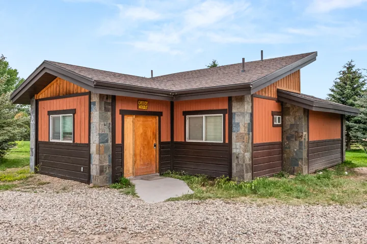 Contemporary exterior featuring stone facade accents, cedar siding, a natural wood entry door, and a gravel foreground