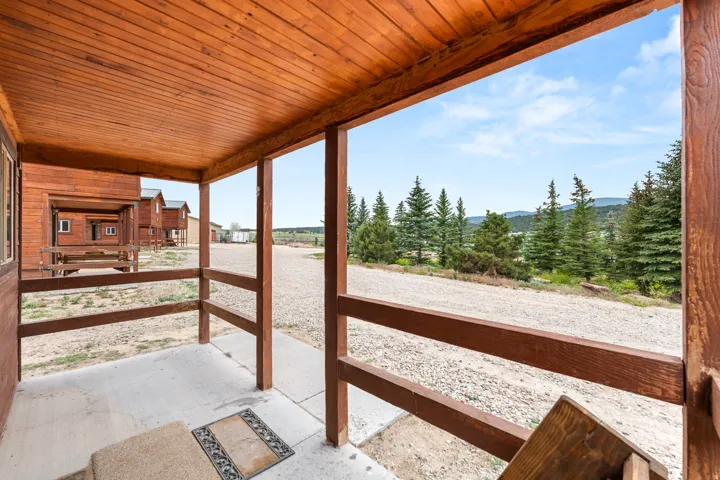 Covered porch with wood-finish ceiling and railing, concrete flooring, and views of mature evergreen trees and distant mountains