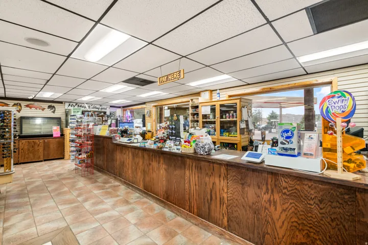 Retail space featuring a wood-finish sales counter, tiled flooring, drop ceiling with integrated lighting, and a large window