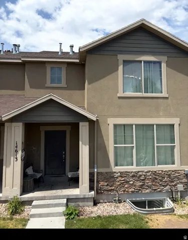 Two-story townhome exterior featuring an inviting covered porch, stucco siding, and stone veneer accents